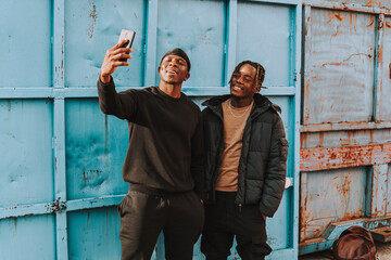 Dos chicos negros tomándose selfies delante de un container de mercancías azul