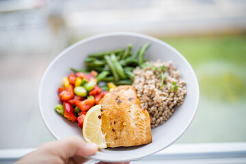 Hand holding salmon and buckwheat dish with green beans