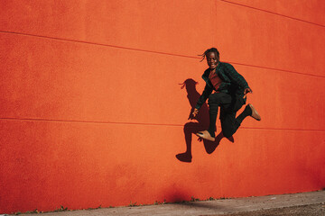 Apuesto hombre español elegante y feliz saltando y posando en el aire en un wallbackground rojo