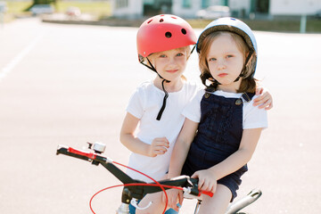 Naklejka premium Two little girls having fun on bicycle. Cheerful sisters in helmets riding outdoors.