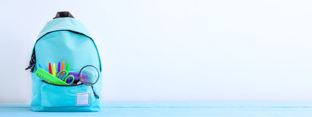 Banner. Concept back to school. Full turquoise School Backpack with stationery on table.