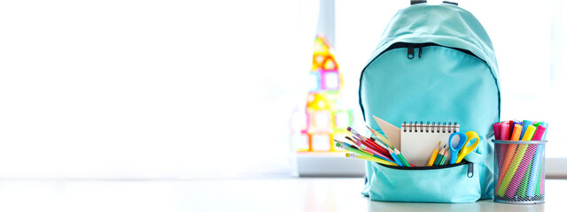 Banner. Concept back to school. Full turquoise School Backpack with stationery on table.