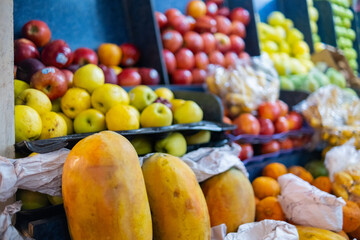 Colorful fruit stand with papayas, red and yellow apples, and more