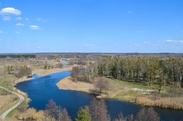 A view  from the top on the river that reflects blue sky, forest, roads, ground underneath. Beautiful landscape scenery from a drone. 