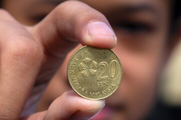 Asian child hand holding a 20 sen Ringgit Malaysia coin, selected focus and blurred background © JakaSuryanta