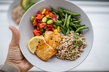 Hand holding salmon and buckwheat dish with green beans