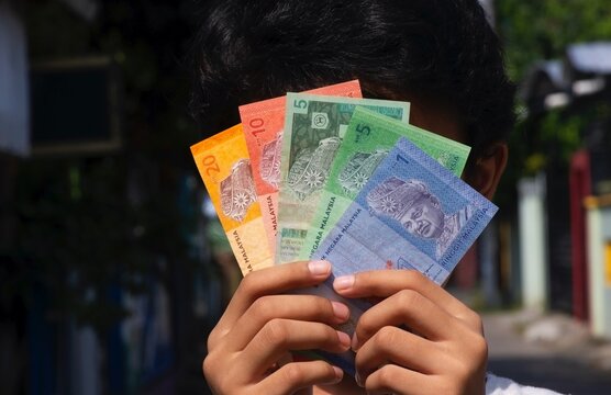 Asian child holding Ringgit Malaysia money in front of his face, selected focus. Concept of salary and inflation
