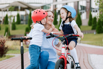 Obraz premium Mother with two cherful daughters having fun. Woman and girls in helmets riding on bicycle and scooter