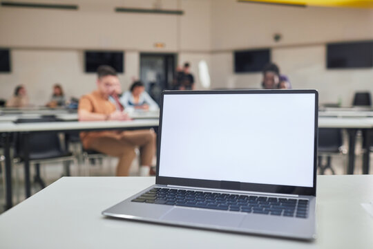 Background image of opened laptop with blank white screen on t5eachers desk in school auditorium, copy space