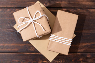 Two gifts in craft paper and an envelope on a dark wooden background, wrapped parcels.