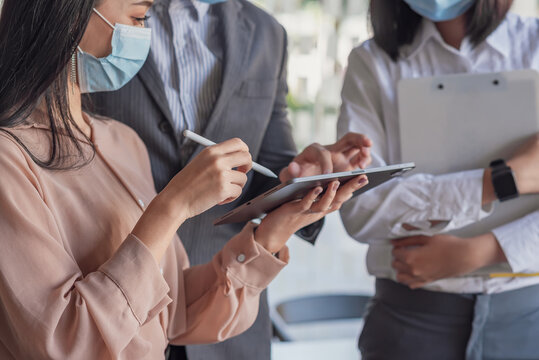 Image of businesswoman working together using a tablet wear a mask to prevent germs at the office.