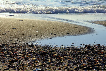 Pebbles, breaking waves and a stream on the sunny sandy beach