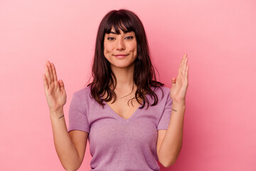 Young caucasian woman isolated on pink background holding something little with forefingers, smiling and confident.