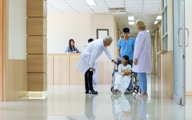 Fototapeta premium Caucasian senior male and female doctors greeting and talking to encourage little girl get injured and sitting on wheelchair in hallway of hospital. Medical Service, Emergency and Insurance Concept.