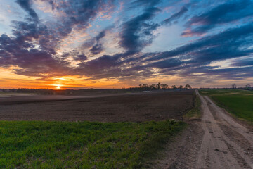 Sunset over rural meadow field and country road. Countryside landscape with path way under Scenic dramatic sky.