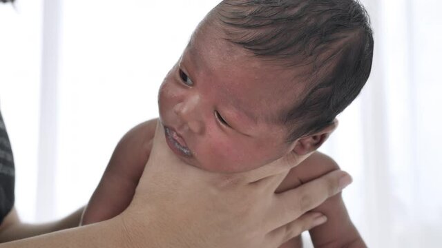 Close up of little baby boy in hand while Mother rubbed on the back of the child to encourage burping after eating full milk, Newborn Mixed race black Ethnicity Thai-Nigeria.