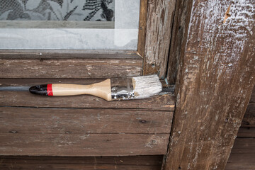 A brush with white paint lies on the window of an old wooden house