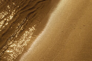 Naklejka na ściany i meble Background with a line of water and a golden sandy beach. The water sparkles in the sun.