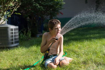 Young boy with Autism playing with garden hose in his backyard; summer time in the Midwest air conditioner outside