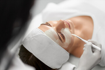 Side view of beautician in white rubber gloves doing peeling face for young attractive patient. Concept of special beauty procedure for improvements skin face and all body.