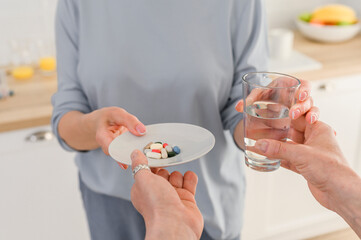Close up senior female hands holding glass of water and taking set of supplement vitamins and pills