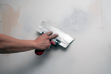 The hand of the builder puttying the wall with putty, leveling the wall with a spatula