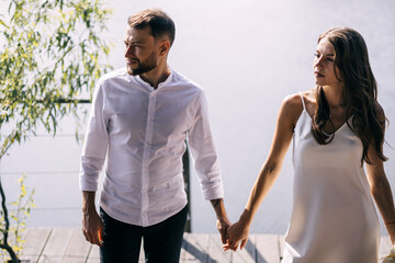 Newlyweds at the pier. The bride and groom walk along the pier to hold hands, in fashionable...