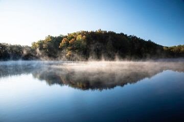 Perfect mirror images of woods reflected in a clear lake. with fog rising. - 431550380
