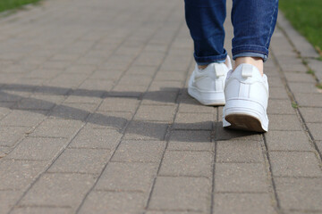 Feet of a girl, walking in white sneakers on the asphalt