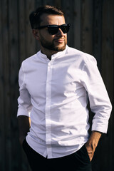 Handsome confident mature man with glasses stands on a wooden brown background. fashionable rich man dressed in expensive clothes posing outdoors.