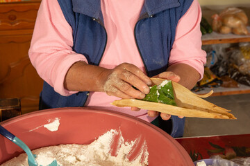 Indigenous woman preparing tamales with masa, stuffed with vegetables, covered by a corn leaf,...