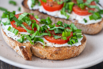 Delicious toasted bread with white cream cheese, green wild garlic and tomato on plate, close up