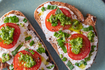 Delicious toasted bread with white cream cheese, green wild garlic and tomato on plate, close up