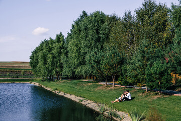 A couple in love lies on the green grass near the water. Embrace. A young girl with curly hair and her boyfriend are relaxing in the open air.