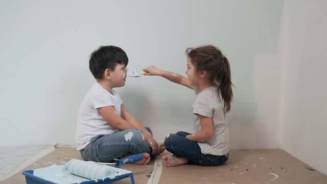 Caucasian kids paint the walls Boy and girl took a break and have fun Girl paints a brush on the boy's face The twins laugh Funny kids Happy family Slow motion