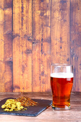 Pint glass filled with beer at the side of a slate filled with hops and brewers barley malt