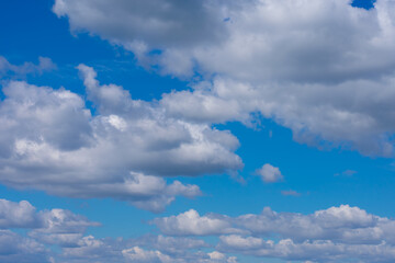 Naklejka na ściany i meble A lot of white fluffy cumulus clouds on bright summer blue sky. Cloudscape, overcast.