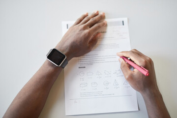 Top view closeup of unrecognizable African-American boy writing in notebook while taking math test in school, focus on smartwatch, copy space