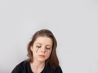 Portrait 15 yo teenage girl with her eyes closed,tears painted aqua gray colors,brown hair loose,black T-shirt.Concept of sadness and loneliness,unhappy non-reciprocal love in adolescence.Copy space