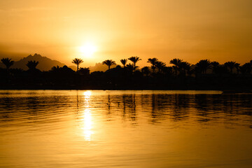 Fototapeta na wymiar Sunset on the sea with mountain view and palm trees