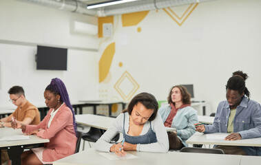 Wide angle view at diverse group of students sitting at desks in school class with focus on young African-American woman in front, copy space