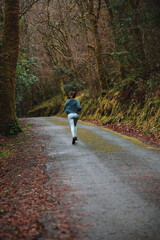 Unrecognizable woman jogging on rural road in autumn park
