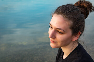 Portrait of a beautiful natural young woman with a hair bun looking into the distance, water background