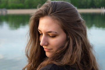 Portrait of a beautiful  natural young woman with a thick hair, looking down, river water background