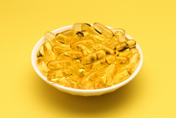 Fish oil gel capsules isolated in white dish on yellow background. Salmon fish capsules view. Omega 3. Vitamin E. 