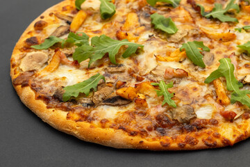 Closeup of a round pizza with cheese, chicken, mushrooms and arugula and spinach on a gray background.