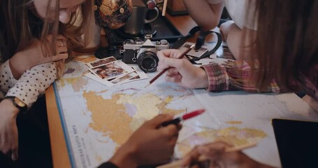 Close-up young happy diverse friends chat, study and look over kitchen table with world map planning travel slow motion.