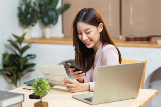 Young Asian female paying online bill with her credit card in laptop while sitting in living room at home. Woman with shopping online payment banking concept