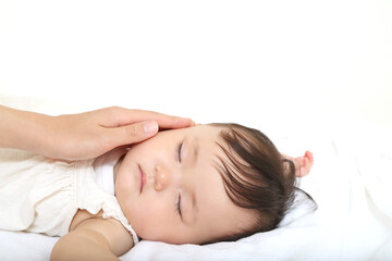 Fototapeta na wymiar 白背景で寝ている赤ちゃんの頬を優しく触れる母の手のクローズアップ。育児、愛情、母性イメージ
