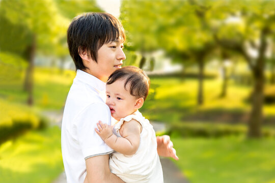 新緑の樹木を背景に赤ちゃんを抱くお父さん。幸せ,愛情,育児イメージ